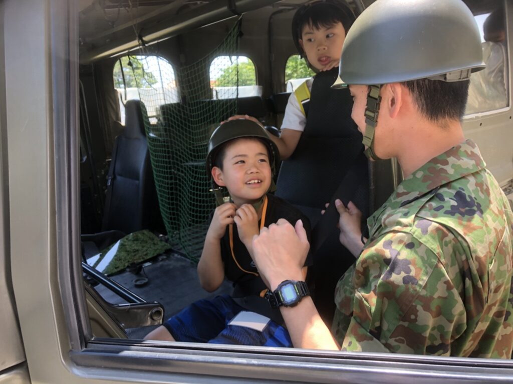 車両に乗り込みヘルメットをかぶる子どもと隊員